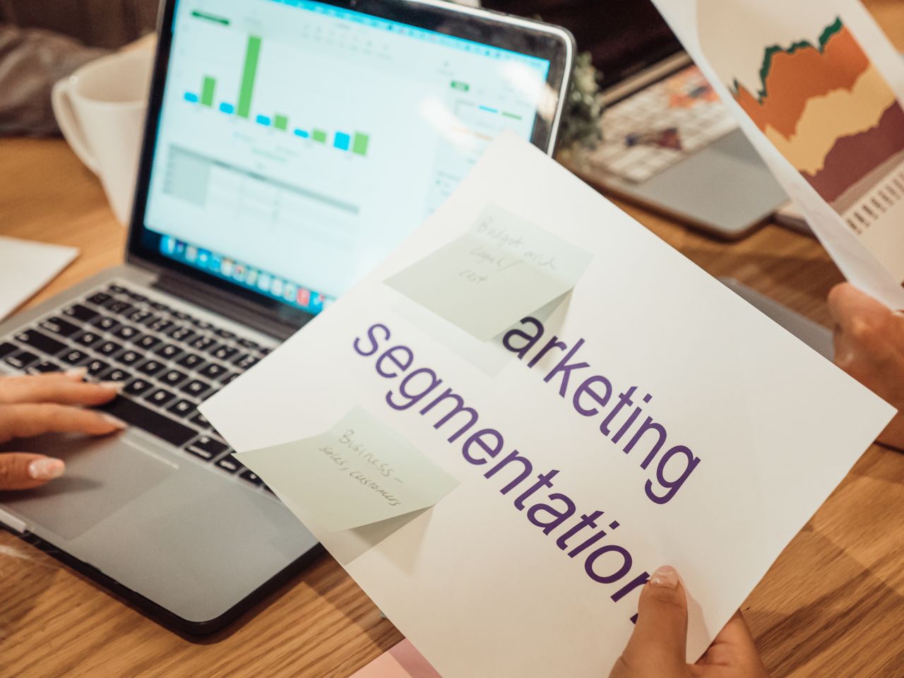 A contemporary workspace with hands reviewing marketing data on a laptop alongside paper documents.